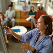 Asian female manager leading a presentation in the office while the rest of the team sits on the sofa listening attentively.